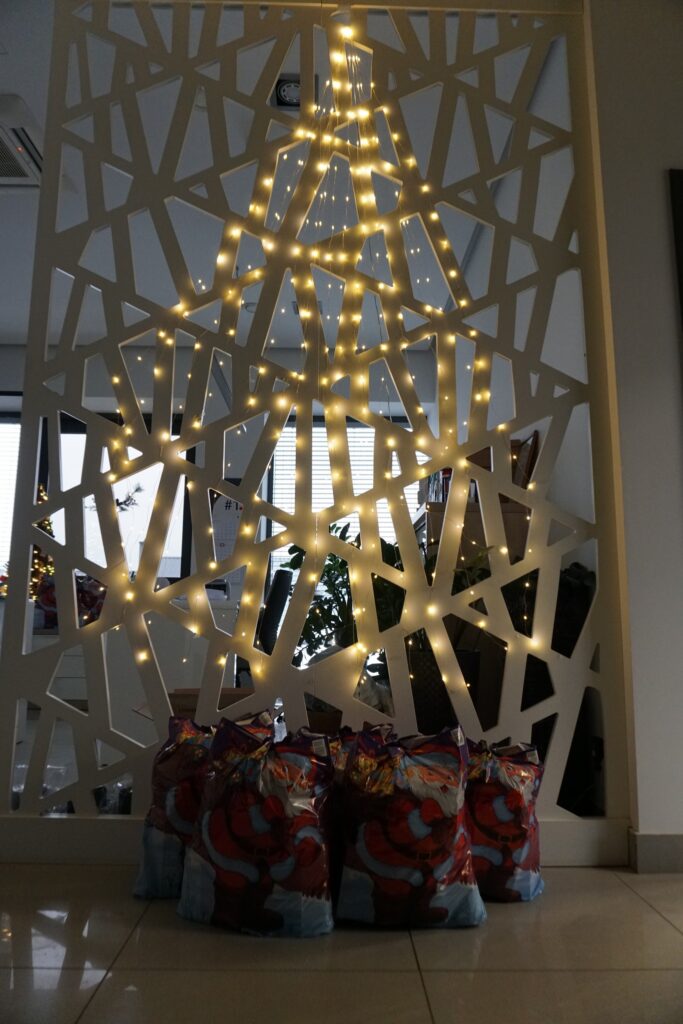 Świąteczne paczki Turhen ustawione pod dekoracją świetlną w kształcie choinki w biurze, przygotowane dla dzieci pracowników.