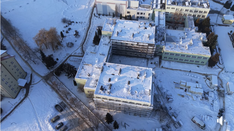 Widok z drona na termomodernizację szkoły w Kwidzynie zimą, ukazujący ocieplane budynki, rusztowania oraz zaśnieżony teren inwestycji.